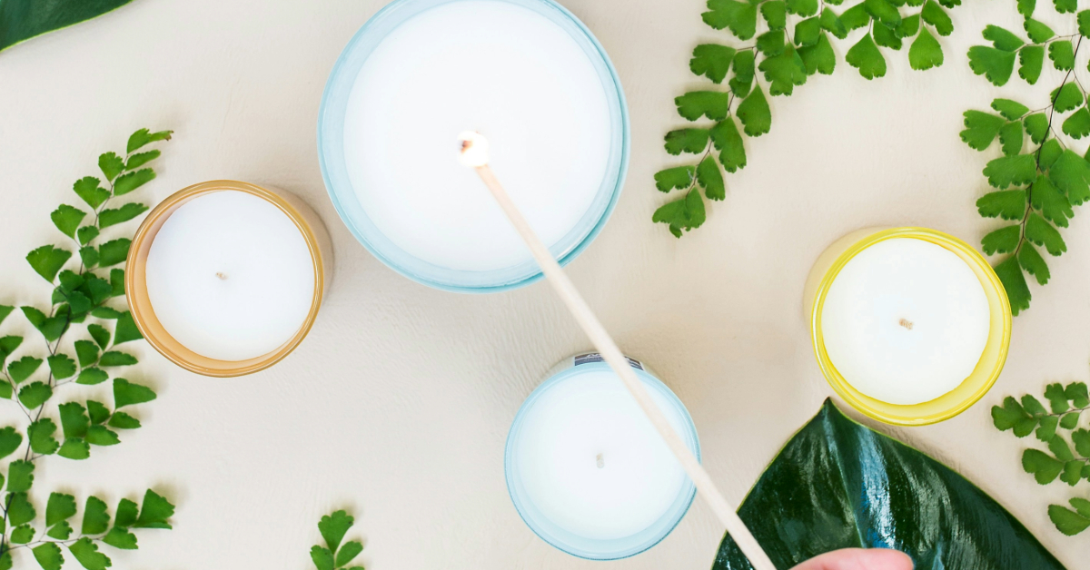 Four candles being lit with long match surrounded by fern plants